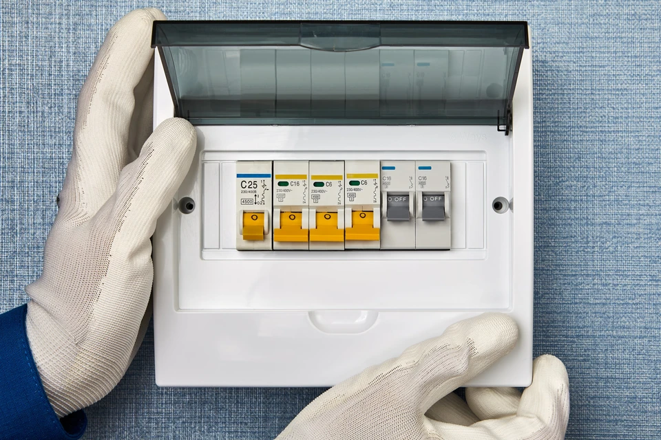 Électricien en gants blancs manipule un tableau électrique domestique ouvert