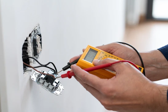 Électricien professionnel en gants de protection installant des prises électriques murales dans un intérieur résidentiel